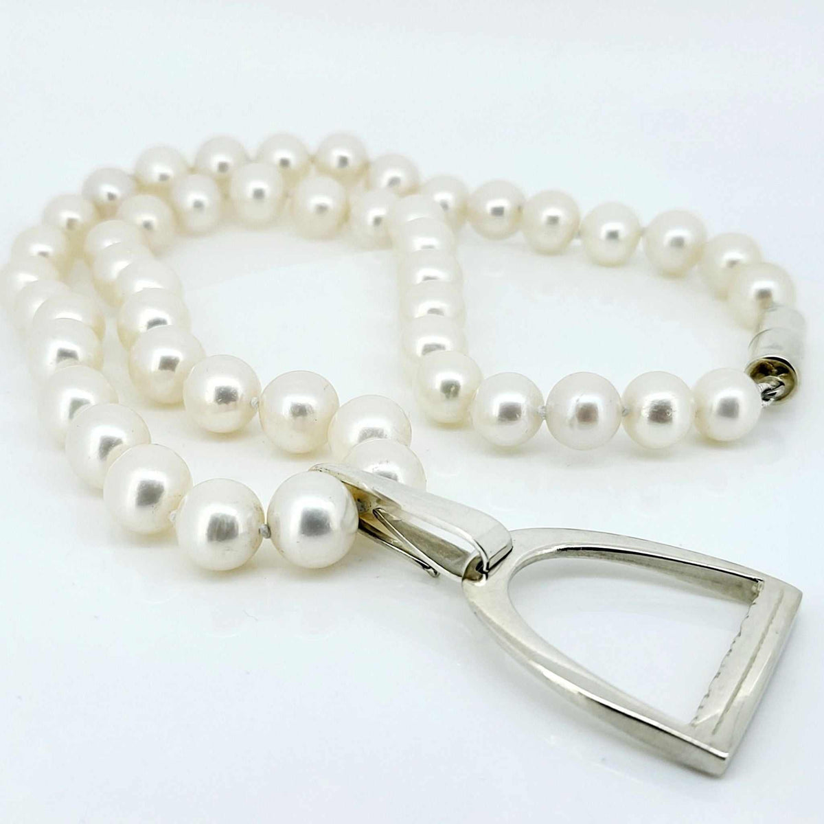 This is a photo of a large Stirrup Pendant, made from sterling silver, attached to a string of white pearls made by Crawford Hill Equestrian Jewellery.