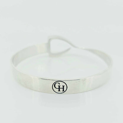 Equestrian Bangle in polished silver-tone metal with a smooth oval band and a small black circular monogram detail