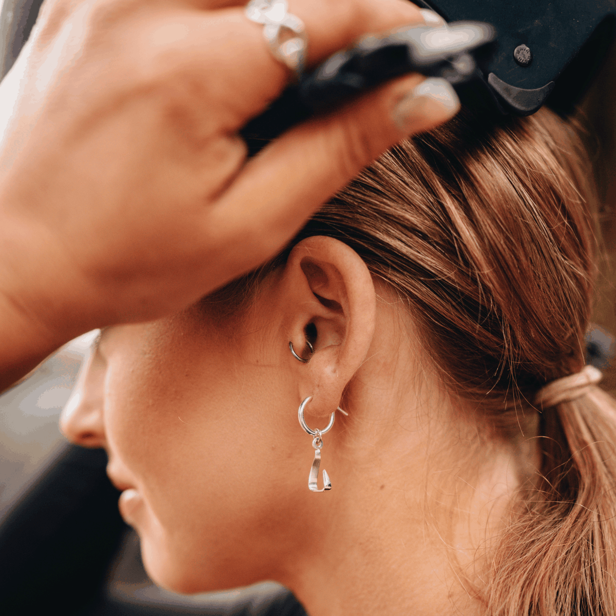 Equestrian Earrings in polished silver feature a small hinged huggie hoop with a dangling stirrup charm.