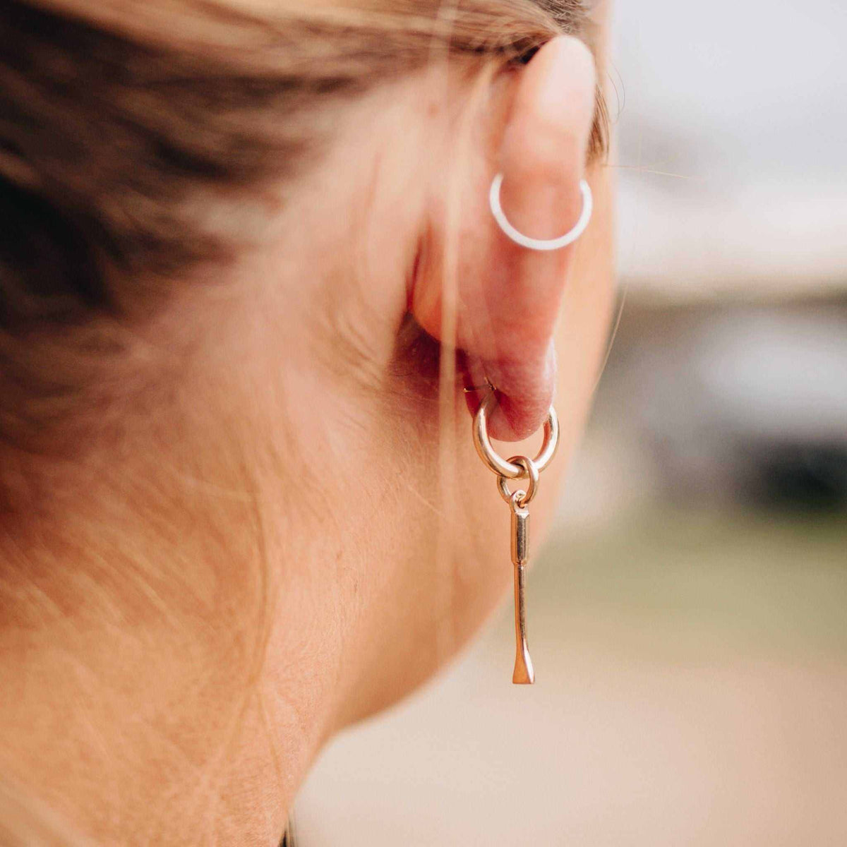 Equestrian Earrings in polished silver-tone metal, featuring a small huggie hoop with a slender stirrup-shaped dangling charm.