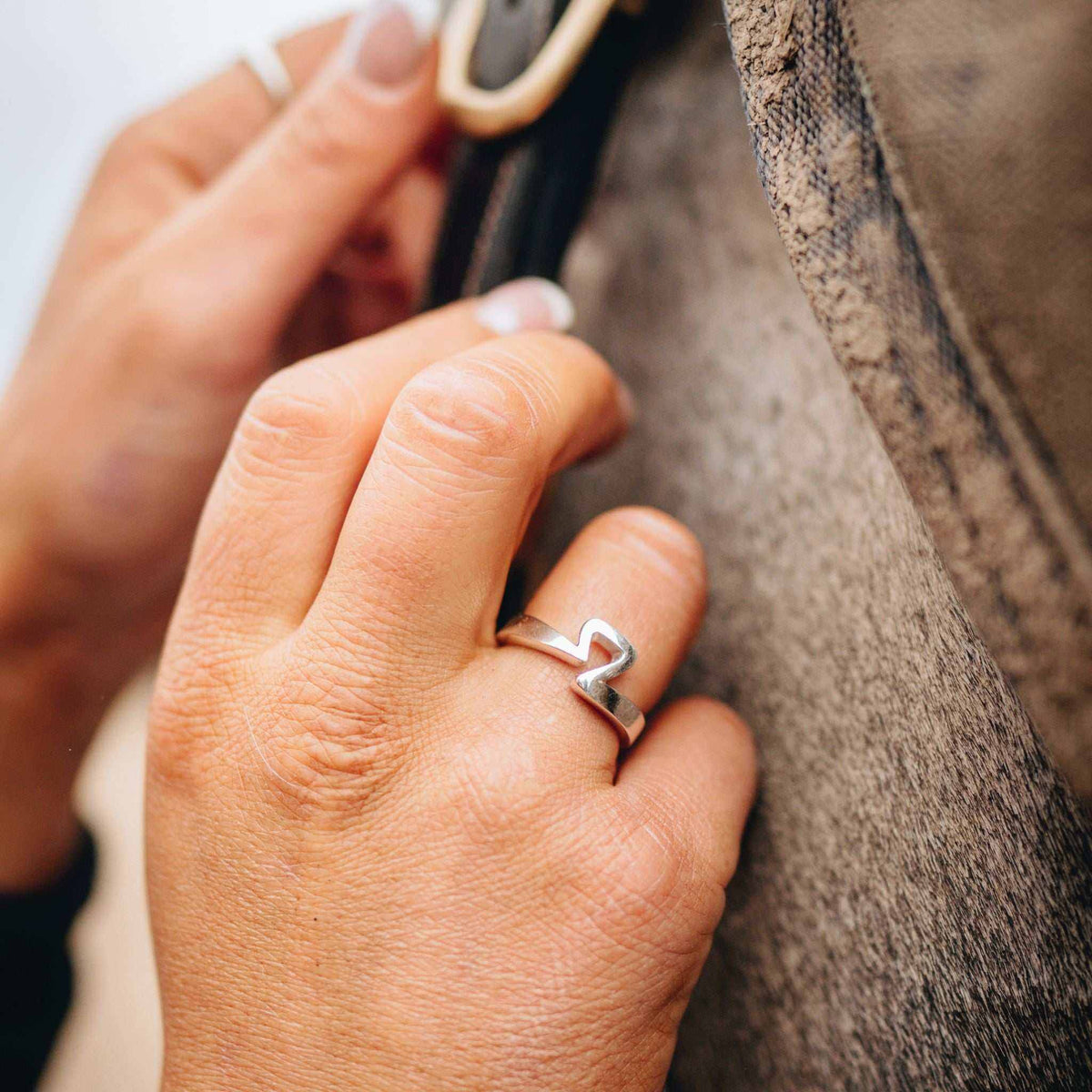 Equestrian Ring in polished silver, worn on a hand, with a distinctive open band shaped like a stirrup