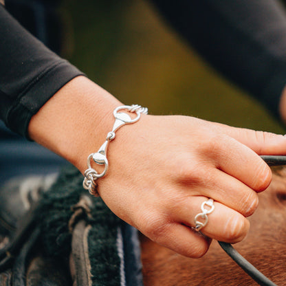 Horse rider holding the reins while riding a horse wearing a horse bit snaffle curb chain bracelet and a horse bit snaffle ring made by Crawford Hill Equestrian Jewellery. 