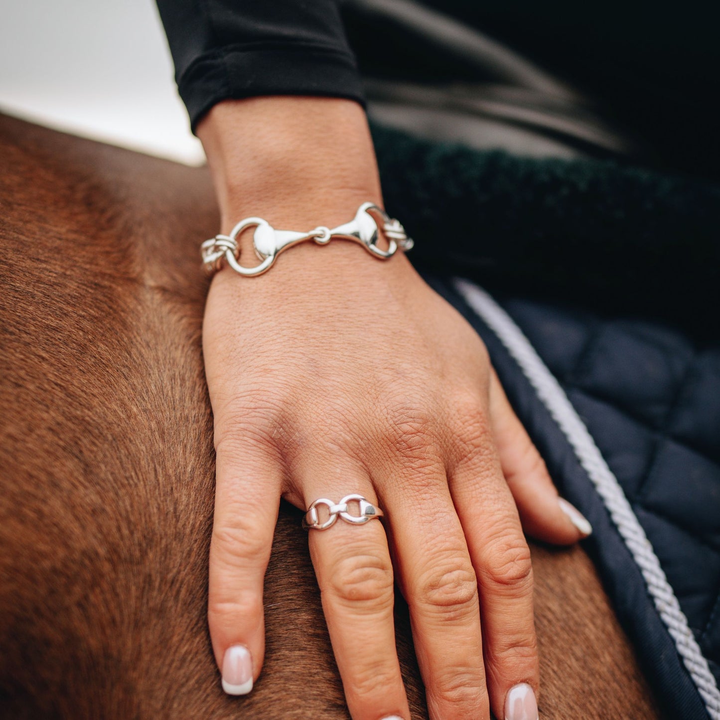 A horse rider patting a horse, wearing a horse bit snaffle curb chain bracelet paired with a horse bit snaffle ring. Both made by Crawford Hill Equestrian Jewellery. 