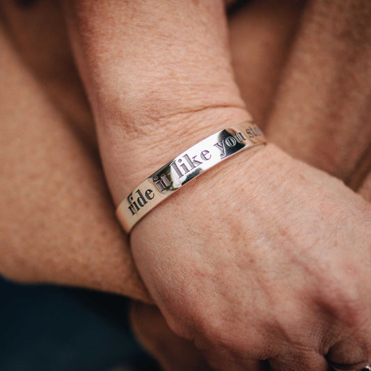 Bangle in polished silver with engraved Ride It Like You Stole It lettering and dark enamel-filled lettering